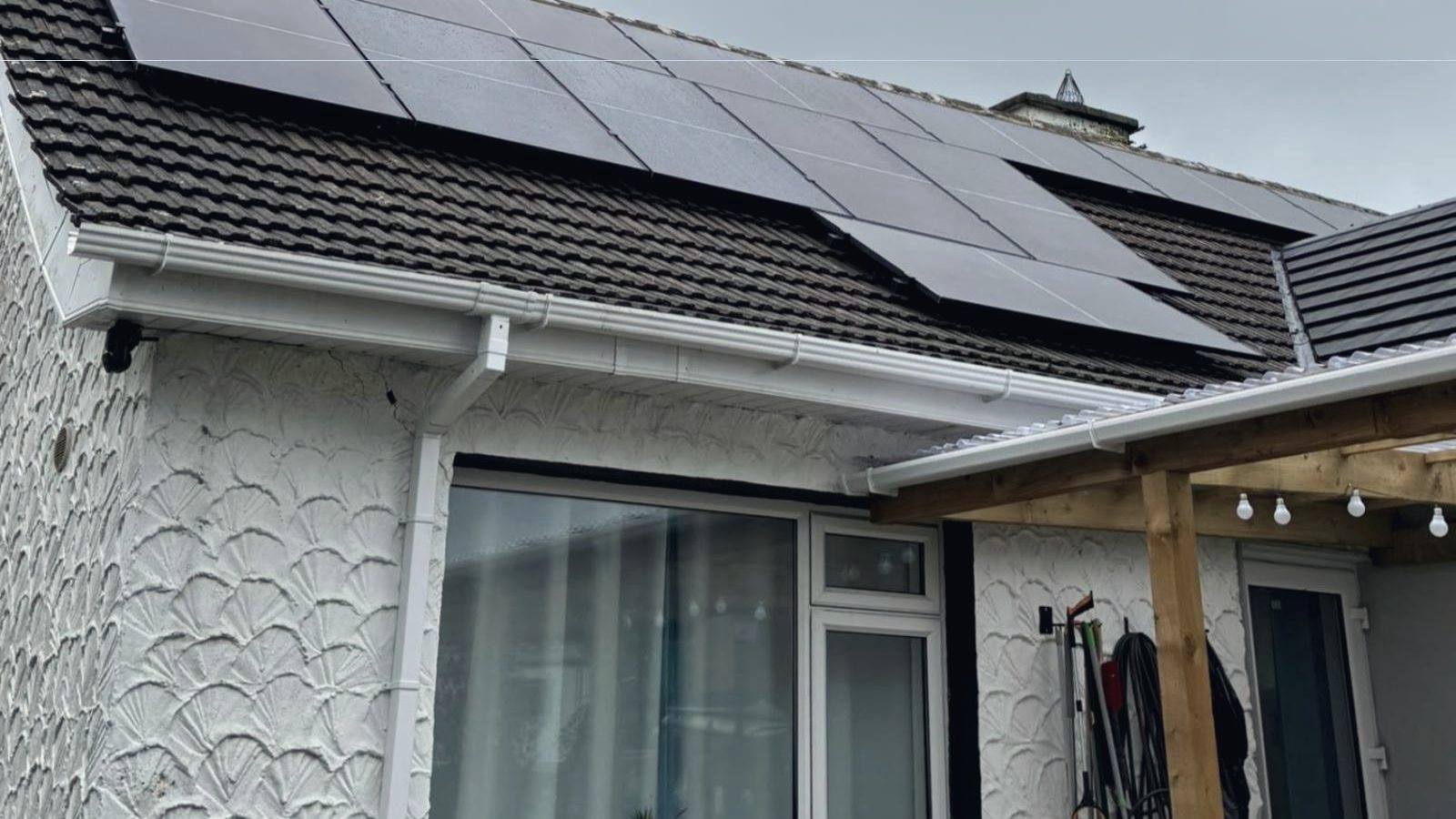 Black solar panels across the tiled roof of a white bungalow under a grey sky
