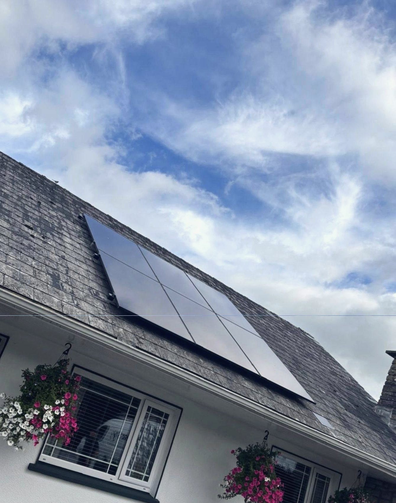 The front of the house with hanging baskets of flowers, and the panels on the slate roof above