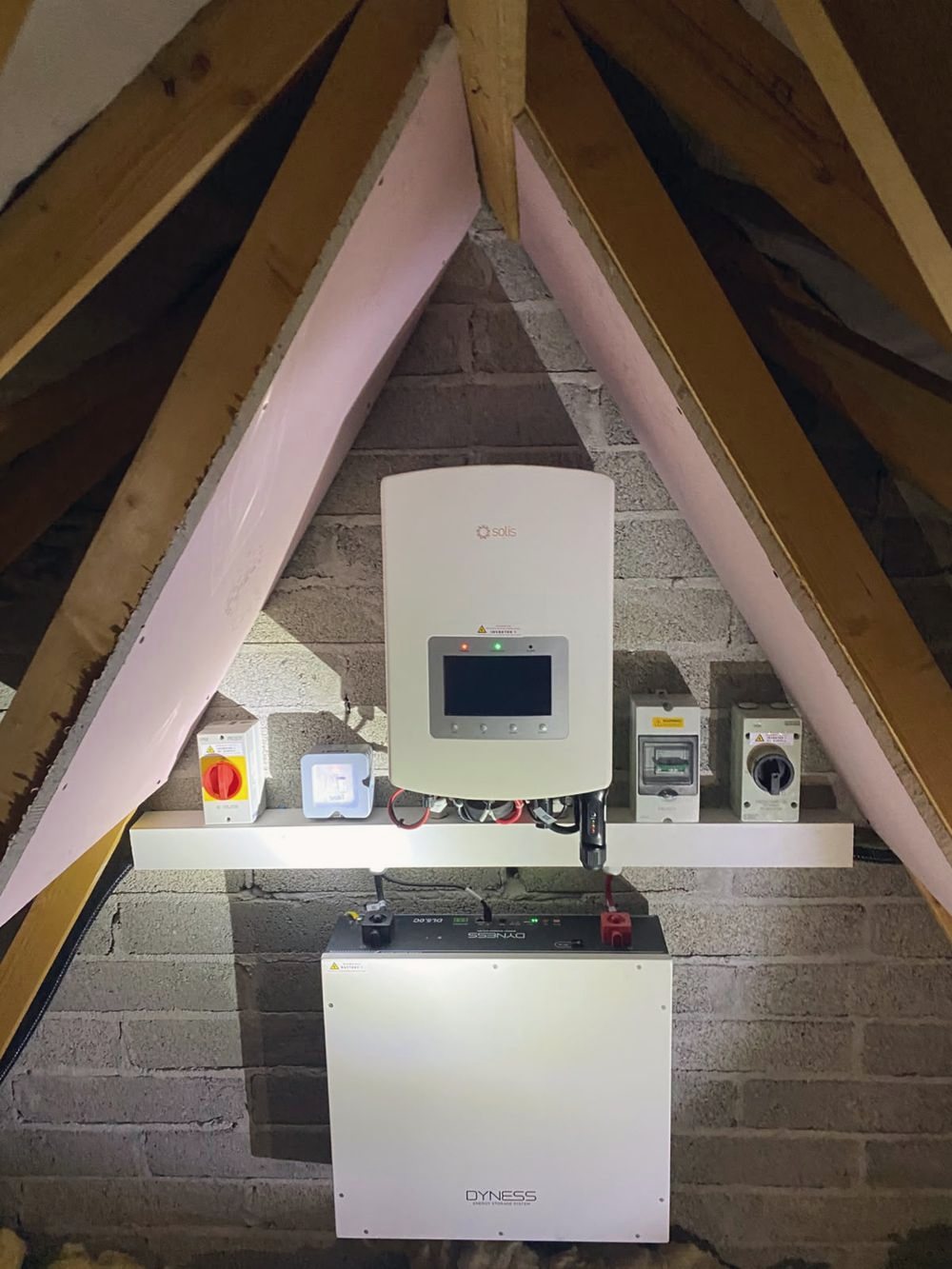 A Solis hybrid inverter and Dyness battery fitted in an attic, with labelled isolators beside it